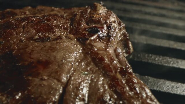 Close up of a juicy t-bone steak sizzling on a hot grill with charred sear marks