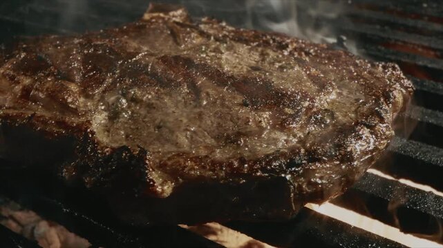 Close up of a juicy seasoned steak sizzling on a hot grill with flames and charred marks
