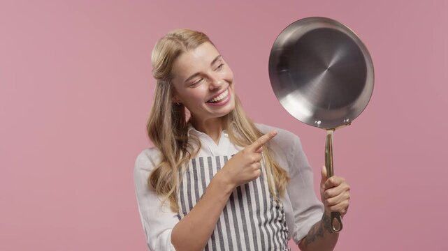 Happy smiling woman pointing at stainless steel frying pan. Eco friendly cookware for healthy food preparation, sustainable kitchen, non toxic cooking, reusable kitchenware and conscious lifestyle