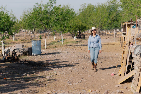 Young woman in cowgirl outfit walking through rural farm.