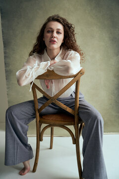 Curly-haired woman in light dress sits on a soft couch