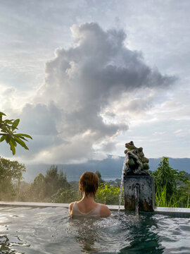 Woman relaxing in outdoor hot spring pool with mountain and cloud view