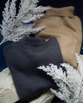 Warm sweaters displayed on a rock with white foliage