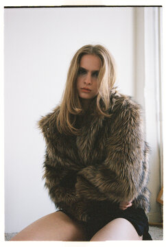 Model sits on the floor wearing a fur coat with long hair