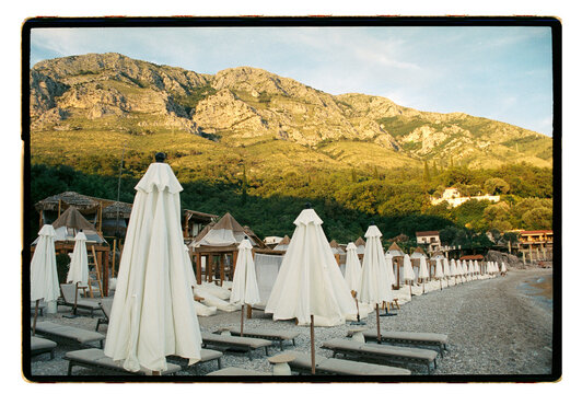 Closed beach umbrellas line a quiet Mediterranean shore at dusk