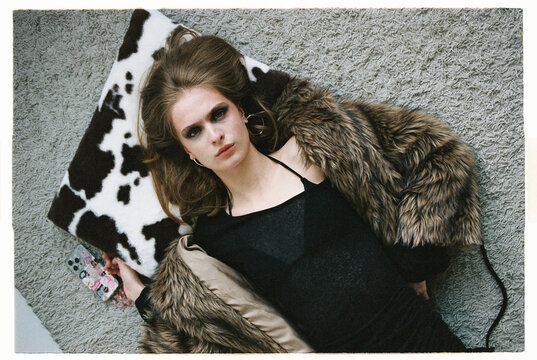 Model lies on a fluffy surface in a black outfit with a fur coat