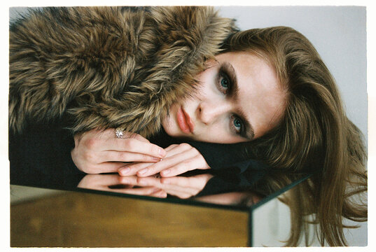 Fashion Model poses with fur coat on a reflective surface indoors
