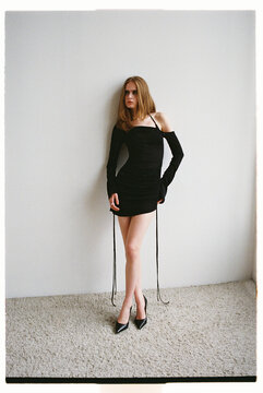 Model poses in black dress near white wall