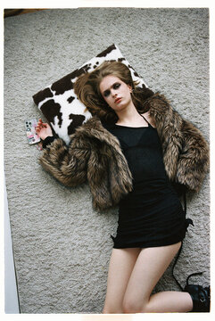 Fashion model lies on a soft rug with a furry coat and black dress