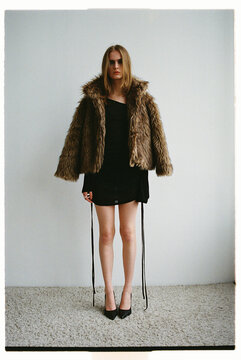 Model stands in a studio wearing a fur coat and black dress