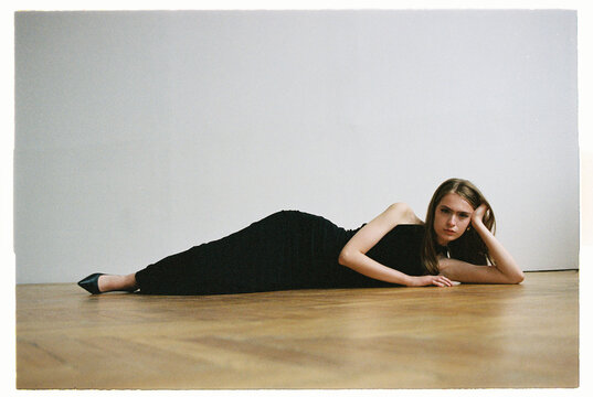Model in black dress rests on floor in indoor studio during daylight