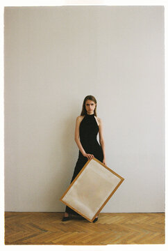 Model stands by the wall holding a large empty frame