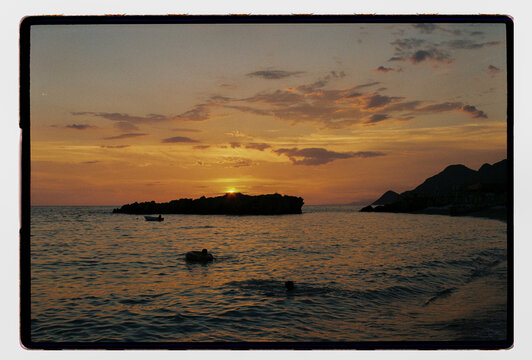Swimmers and small boats at dusk on a rocky Mediterranean bay