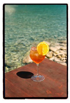 An Aperol spritz on a wooden ledge above clear turquoise water