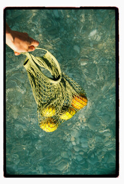 Lemons and oranges dangle in a mesh bag over the sea