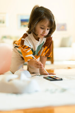 Little kid holding a watercolor brush painting a face mask 