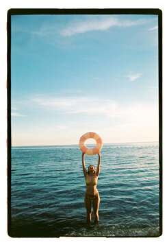 A woman lifts a pink pool ring above the open sea