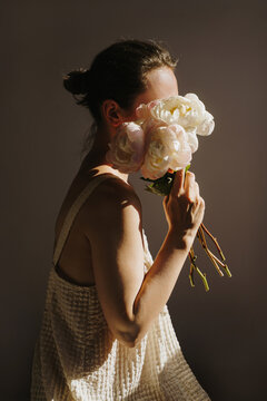 Elegant woman holding bouquet of pale pink peonies in dramatic light