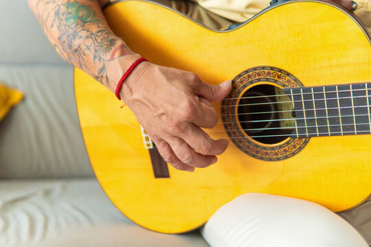Person playing acoustic guitar with tattooed arm