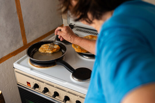 Elderly Woman Frying Traditional Homemade Pastries in Rural Kitchen