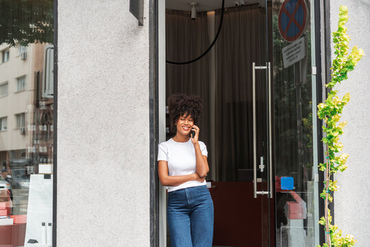 Smiling Woman Standing in Shop Doorway Talking on Phone