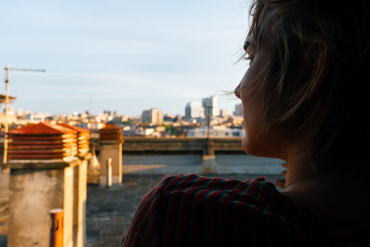 Woman Looking Over City From Open Window At Golden Hour