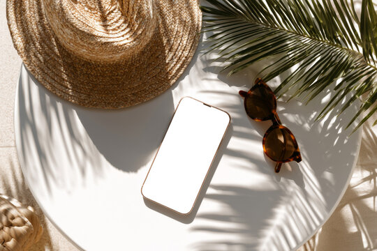 Summer smartphone mockup with straw hat sunglasses and palm leaf shadows on white table