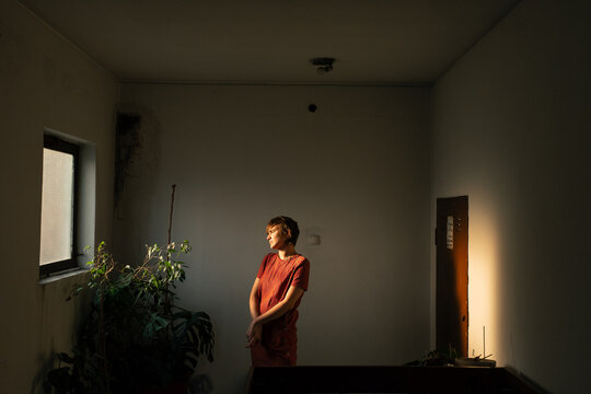 Woman Standing In Warm Window Light Inside Hallway