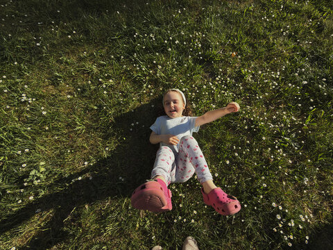 Happy little girl laughing while lying on a green daisy meadow.