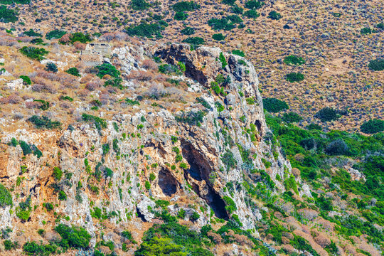 Beautiful view of rugged rocky hillside with caves and tropical vegetation. Crete. Greece.