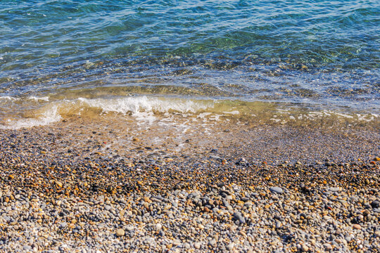 Close-up view of small sea wave washing over pebble beach in sunlight. Crete. Greece.