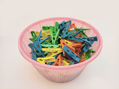 A basket full of clothes pins on the white background, multi color plastic laundry clips or clothes pegs for house