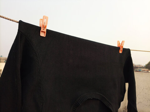 Laundry clips, plastic clothes pins or clothes pegs for house hanging and holding a black sweater on rope on roof top