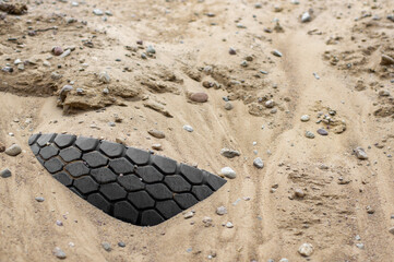 Close-up of a heavy vehicle tire partially buried in loose sand on rough terrain, showing deep tread pattern, wheel tracks and scattered stones. Concept of off-road driving, traction. © Viktoria