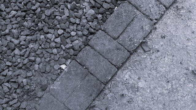 Monochrome ground surface combining crushed gravel, paving stones, and concrete, showing contrasting textures and geometric lines for construction and landscaping concepts.