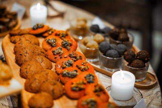 Colorful selection of artisan cookies, seed-topped savory bites and dark energy balls arranged on a bakery counter beside glowing candles with selective focus