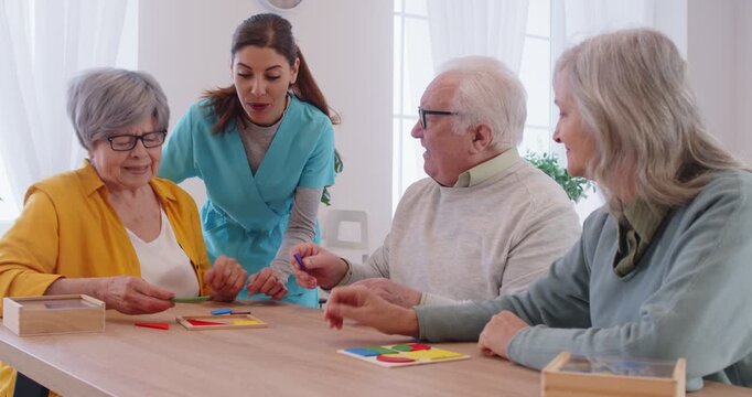 Positive senior patients in a nursing home spending leisure time with a caregiver or nurse, playing a board game together. Engaging in entertainment and building a supportive environment.