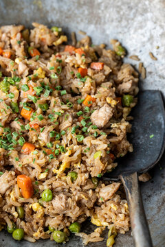 Chicken fried rice in a seasoned carbon steel wok on a dark surface 
