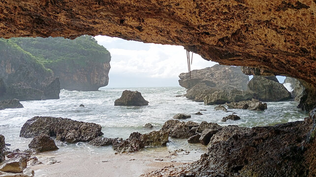 View of ocean waves and rocky beach framed from inside a sea cave rock overhang