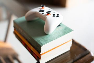 White Xbox Series X controller resting on a stack of colorful books on a wooden table in a cozy © chuangxin