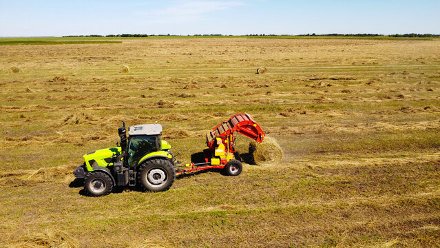 An aerial drone photograph capturing a modern green tractor pulling a red round baler in an open field during hay harvest.