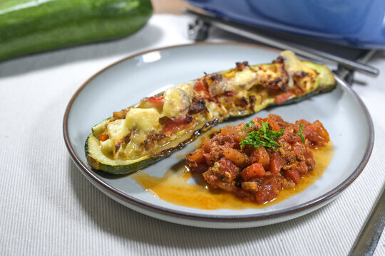 Half oven baked zucchini stuffed with bell pepper, tuna, onions, and feta on a plate served with tomato salsa and parsley garnish, healthy low carb meal, selected focus