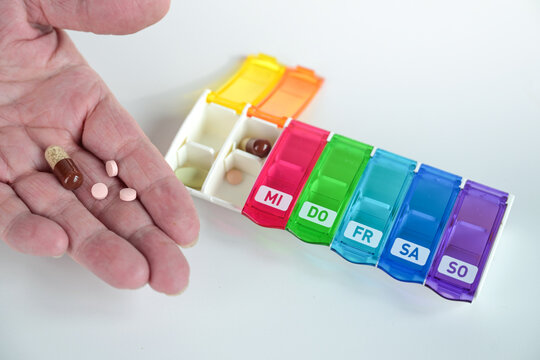 Elderly hand holding medication over a weekly pill organizer, health and medical care concept for people with chronic illnesses or seniors, light gray background, copy space