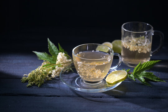 Meadowsweet tea from fresh flowers in two glass cups with lemon slices, medicinal plant (Filipendula ulmaria) used to treat colds, dark blue background, copy space