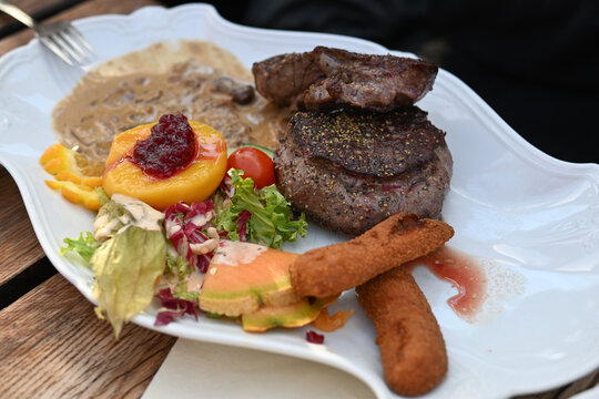 Venison tenderloin fillet steak with croquettes, salad, peach, berries and sauce, main course in a menu on a white plate in a restaurant, selected focus