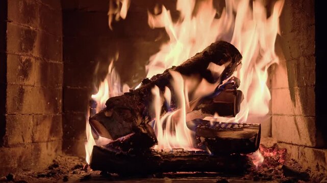 Burning wooden logs with flames and hot glowing embers inside a home fireplace. Cozy winter atmosphere and warm fire indoors.