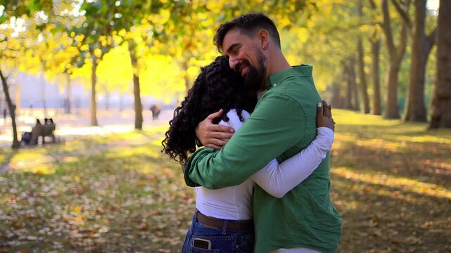 Happy interracial couple sharing a warm hug in an autumn park. Candid outdoor scene with golden sunlight and fallen leaves conveying love, affection, trust and emotional connection