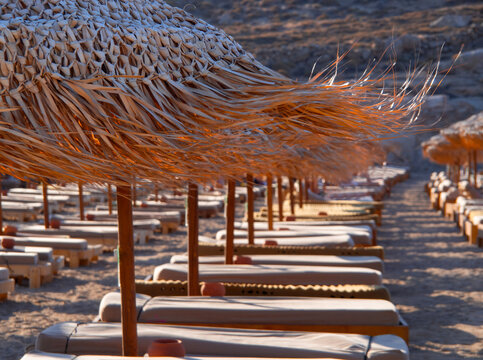 Palm-tree parasols flutter in the wind on a beach on the island of Mykonos in Greece.