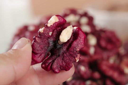 Red-skinned Xinjiang walnut in hand showing natural burgundy coat and cream colored nut meat
