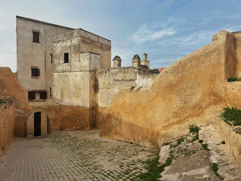 Weathered sandstone bastion walls with rounded sentry towers surround a cobblestone courtyard inside the Portuguese fortress of El Jadida, Morocco.